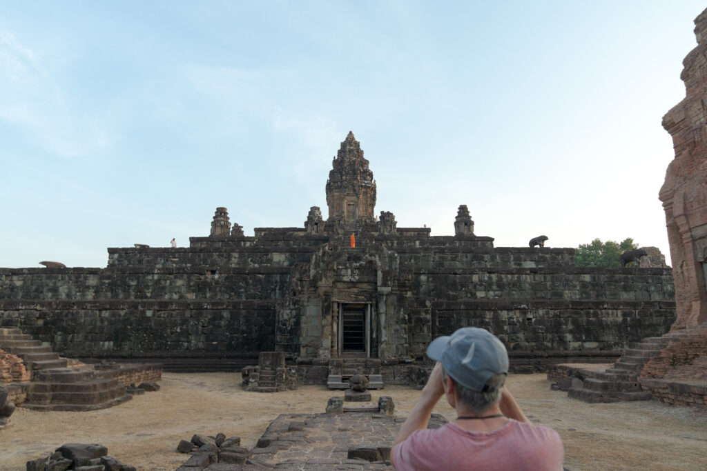 Wide angle view of a Bakong temple with a monk walking along the central stone steps under a clear blue sky