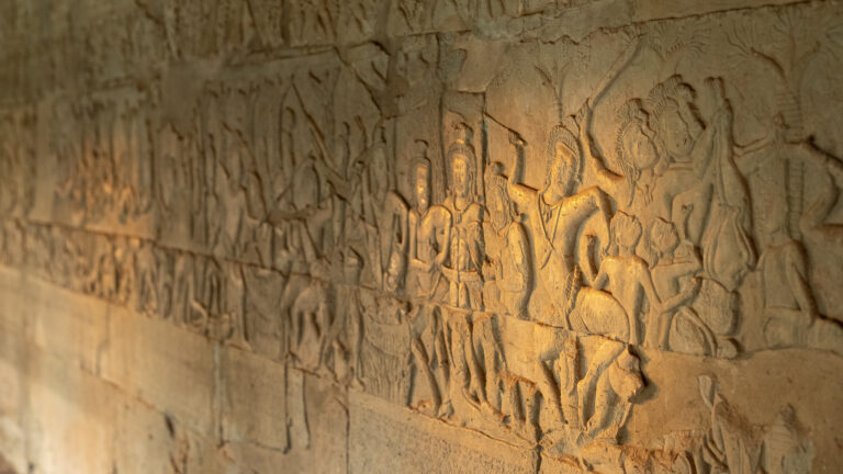 Detailed stone bas-relief carvings of figures inside an Angkor Wat gallery