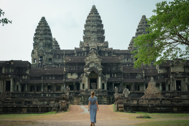 A female visitor walking along the quiet dirt path toward the eastern back entrance towers of Angkor Wat