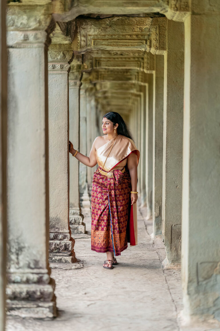 Woman in traditional Cambodian dress walking down a stone pillar corridor during a photoshoot at Angkor Wat