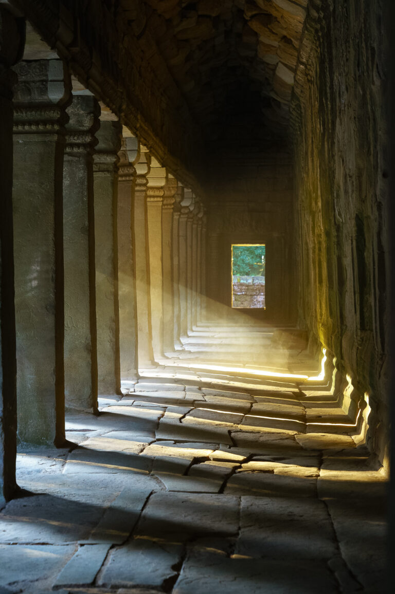 Long stone gallery corridor inside Ta Prohm temple, with repeating columns and sunlight illuminating the ancient floor.