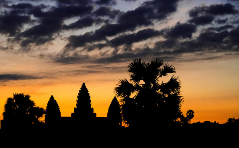 Silhouette of Angkor Wat central towers and sugar palm trees against a dramatic orange dawn sky