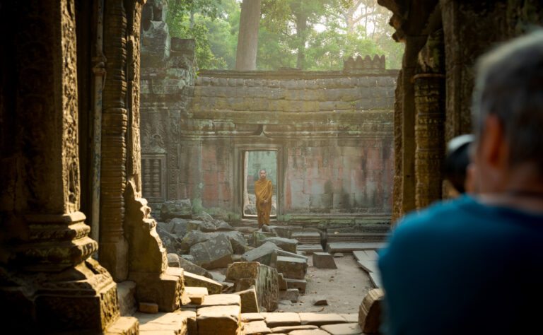 Photographer taking a framed photo of a monk walking through a stone doorway at Ta Prohm temple with Siem Reap Photographer