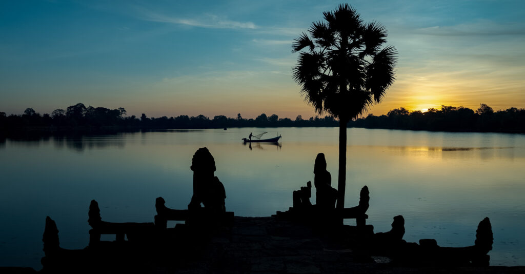 Sunrise over Srah Srang reservoir with a fishing boat and palm tree at Angkor