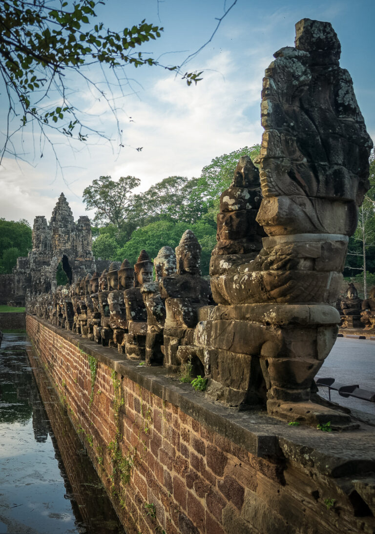 Stone gods and demons lining the causeway to the South Gate of Angkor Thom, with the carved face tower visible beyond