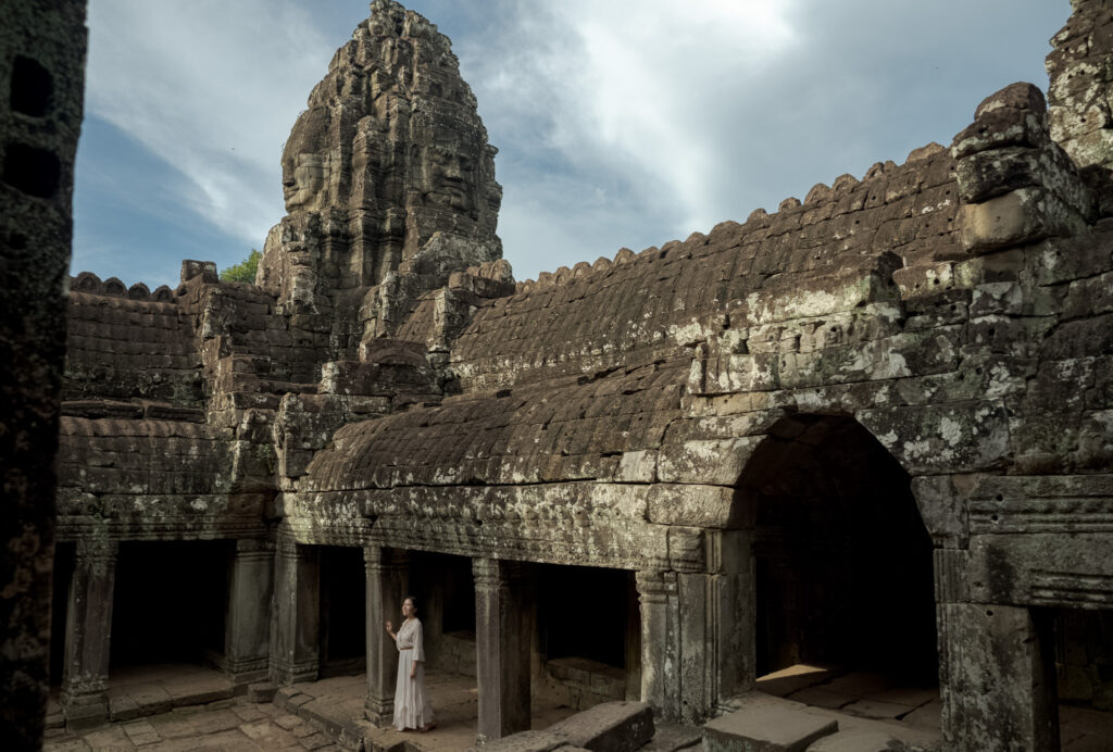 Visitor at Bayon temple with stone face in the distance